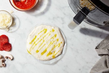 shaped thin-crust pizza crust on a parchment round, drizzled with oil